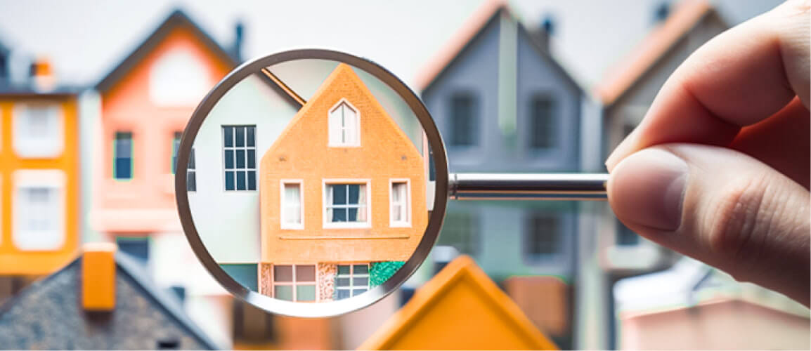 Magnifying glass focusing on a small, orange model house among other colorful model houses.