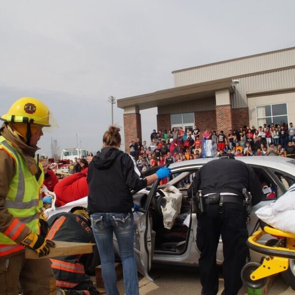 Emergency responders assist at the scene of a car accident with onlookers in the background, near a building labeled "Fine Arts and Civic Center.