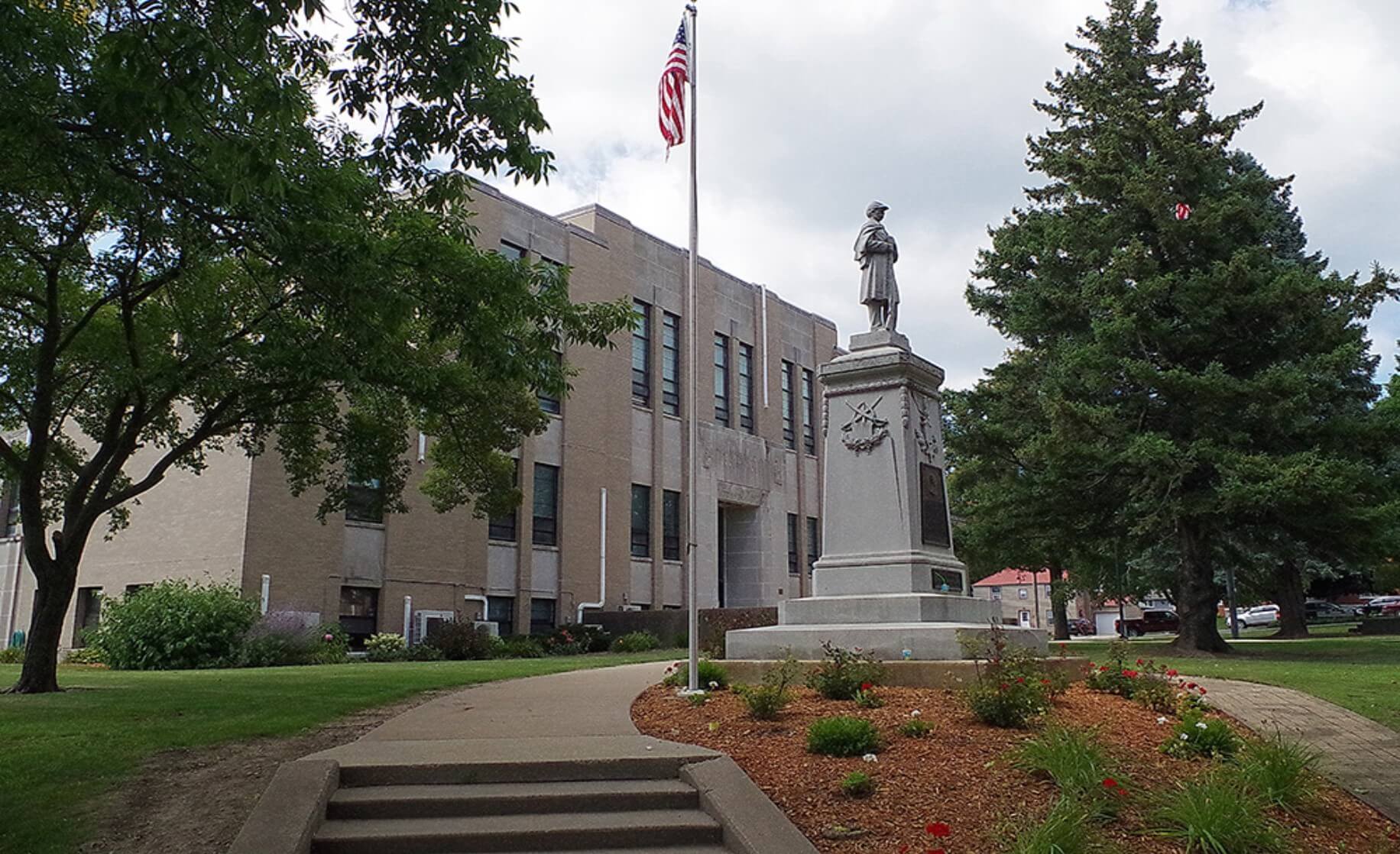 Statue and flagpole in front of a building surrounded by trees and a landscaped garden.